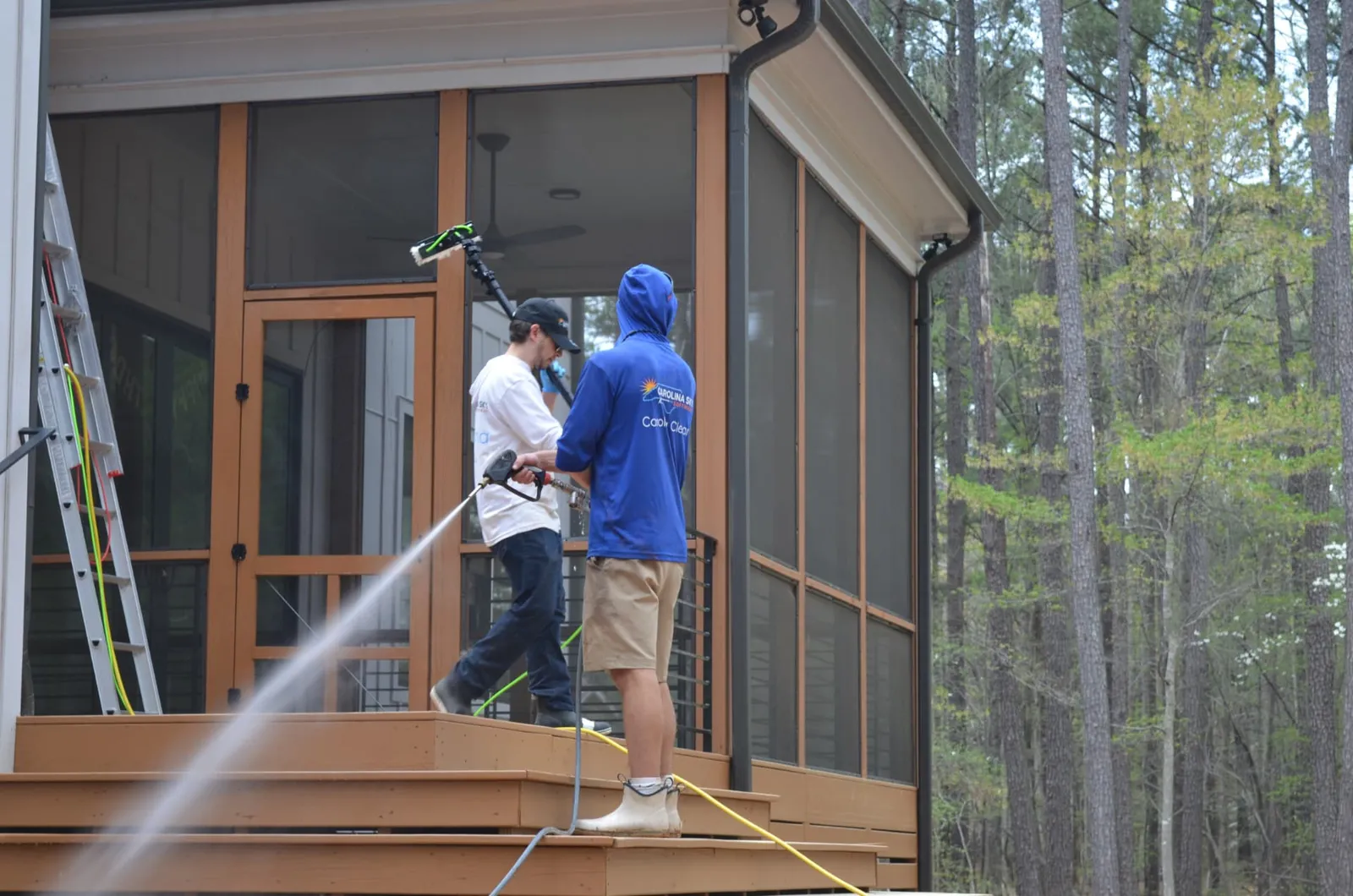 Two technicians washing a wood deck and cleaning screened porch windows