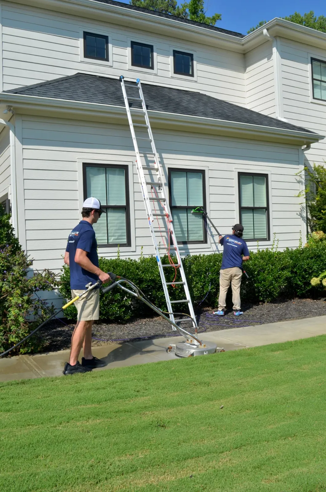 Technicians working around a white house with a ladder and surface cleaner