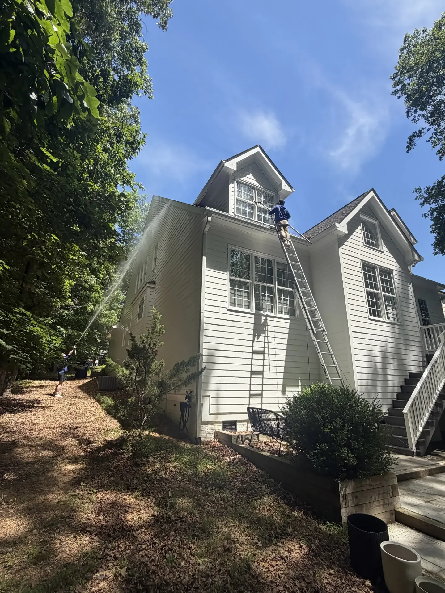 Technician washing farmhouse siding from a ladder during a soft wash house cleaning