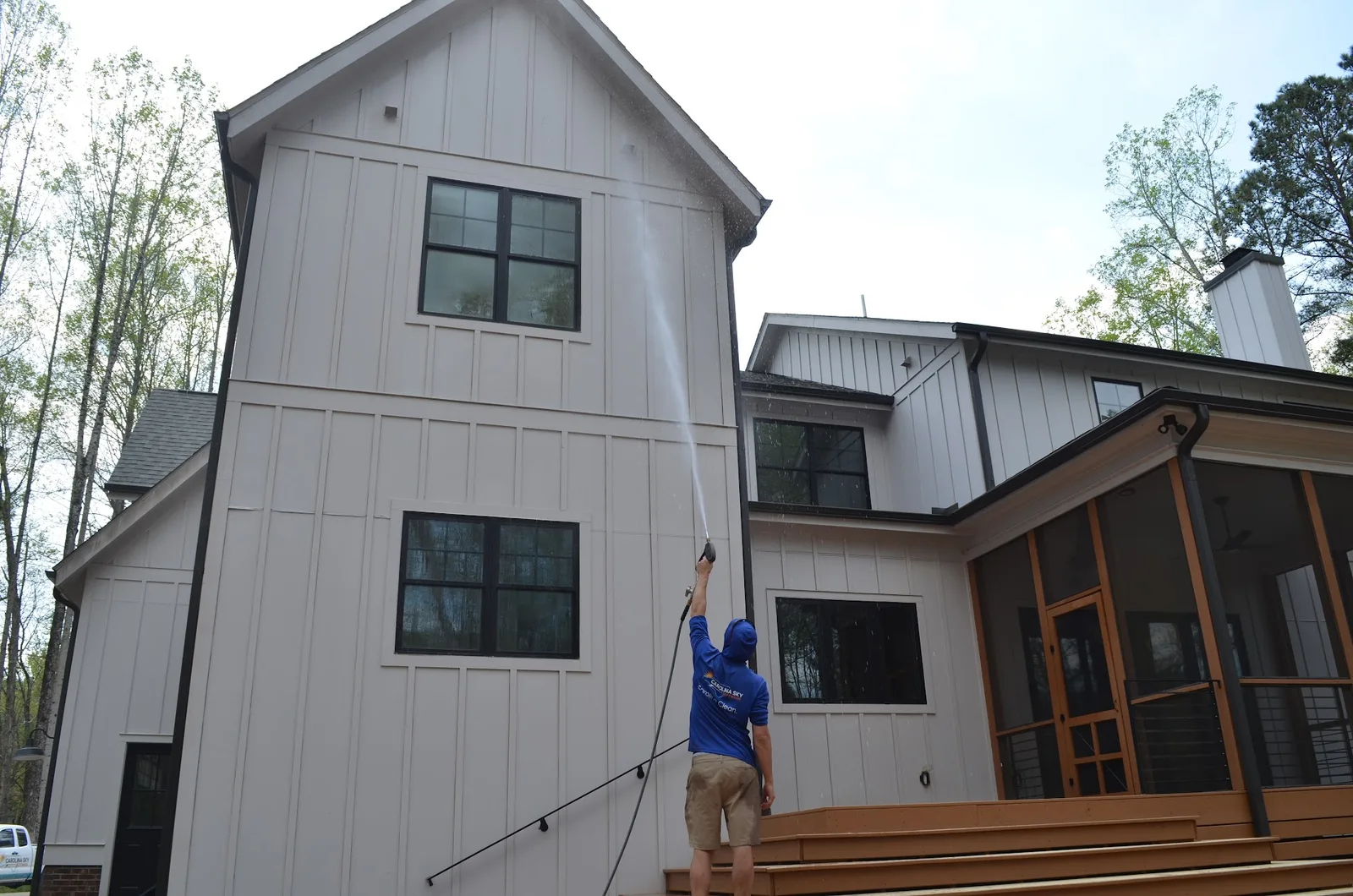 Technician washing farmhouse siding with a spray wand
