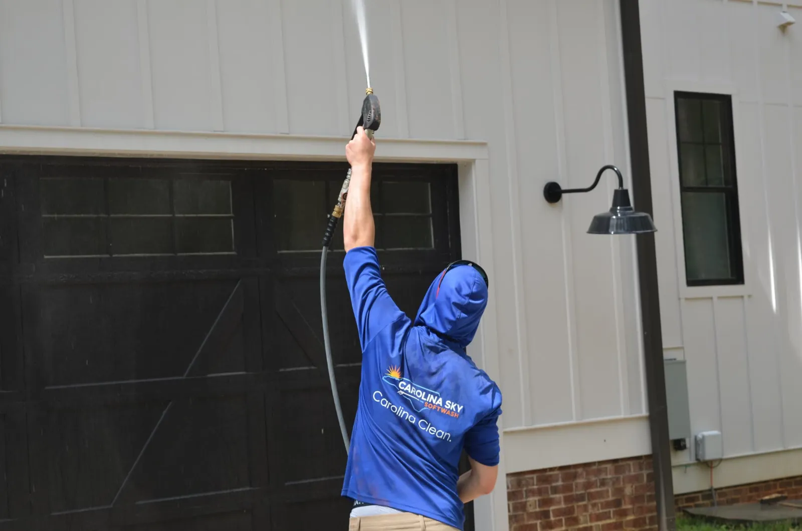 House washing: technician rinsing white board-and-batten siding above a garage door in Chapel Hill, NC