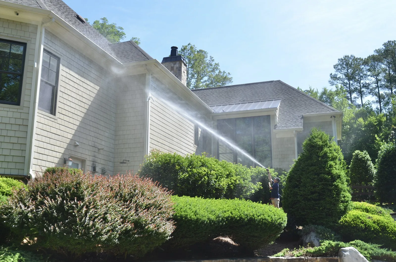 Low-pressure soft wash spray rinsing the siding of a light-colored home