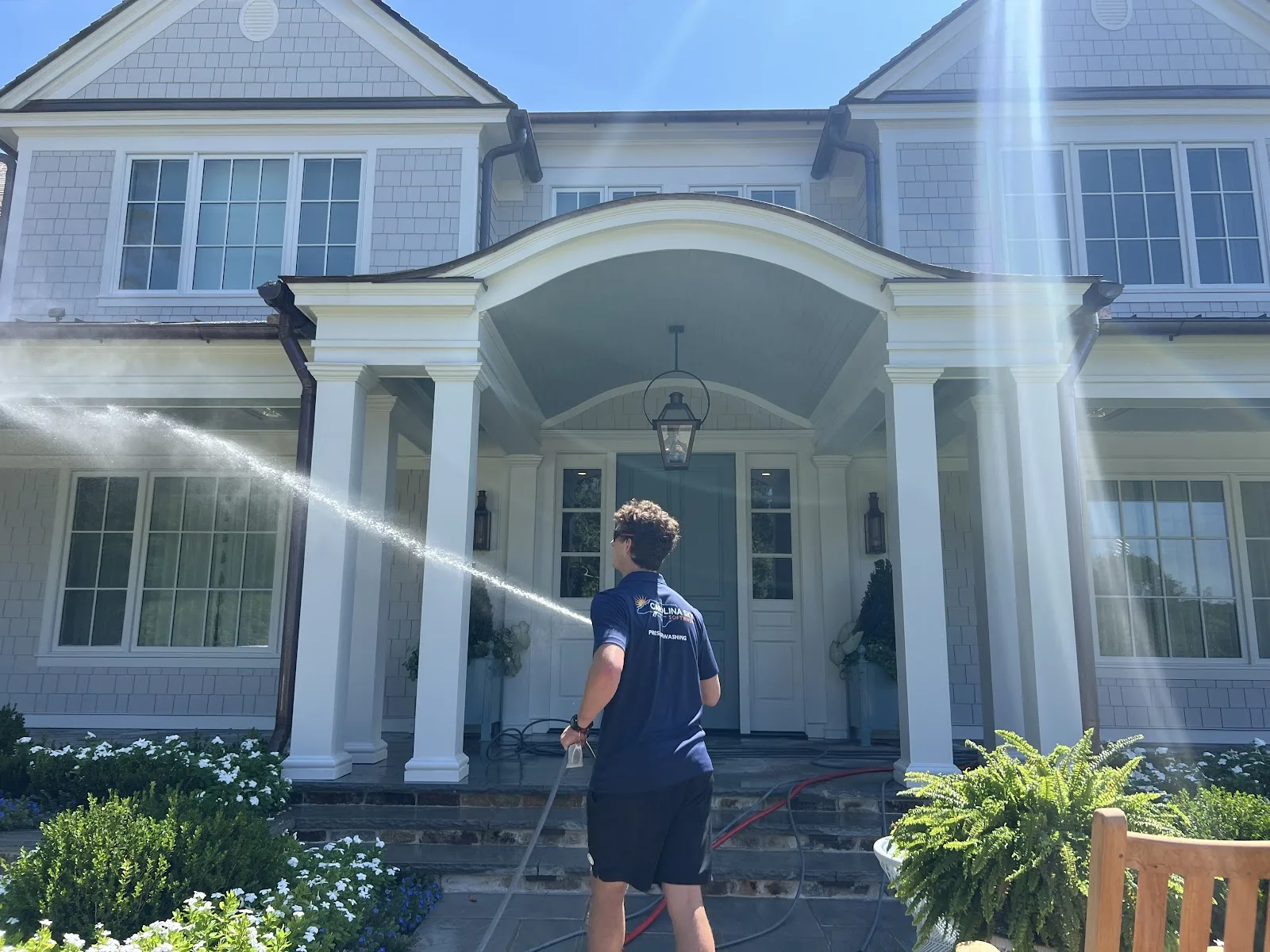 Technician soft washing the entry columns and porch of a two-story home